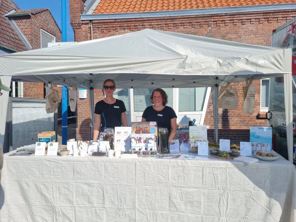 People standing outside behind a table with a lot of informational flyers about algae as food.