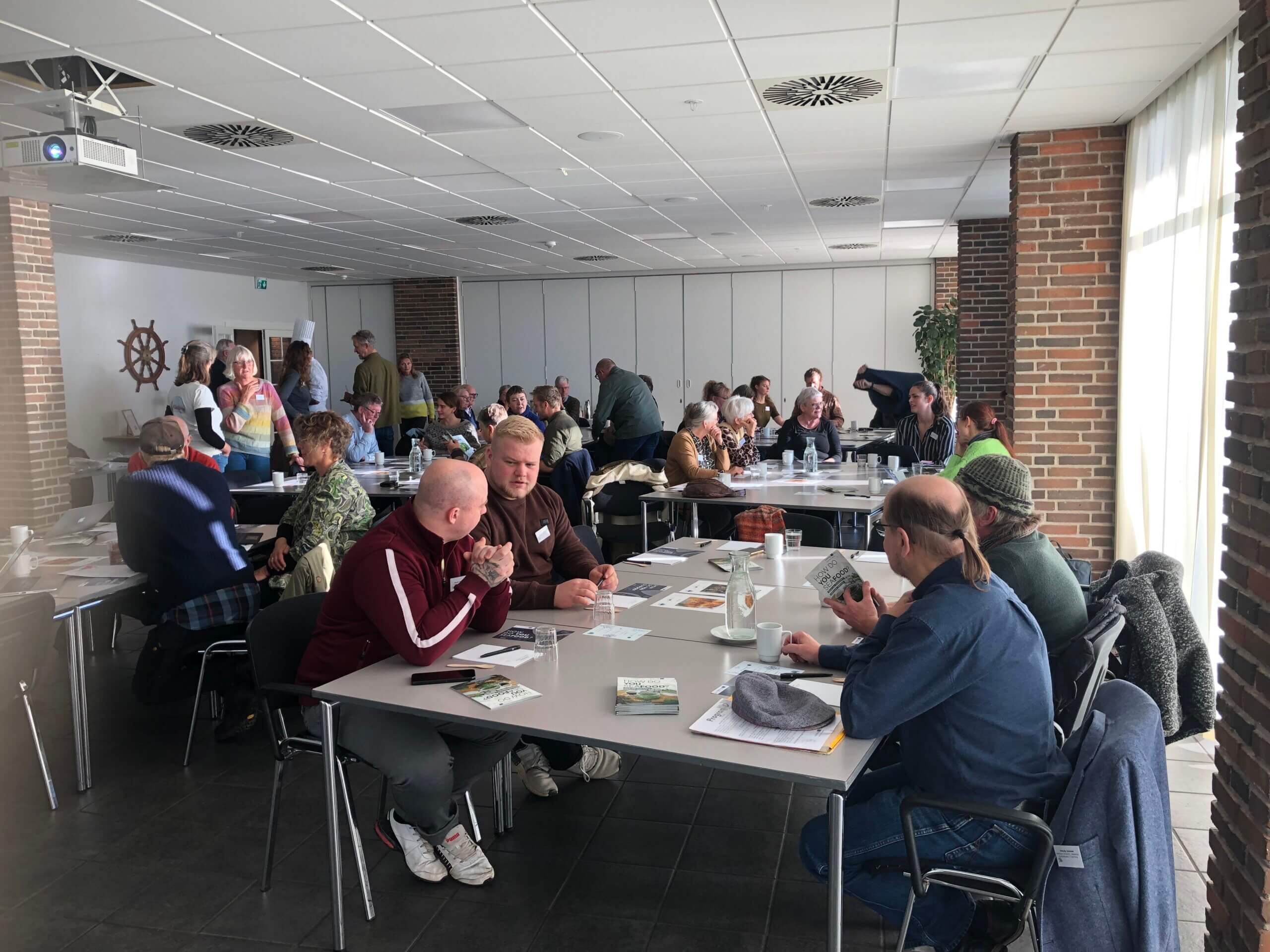 Verschiedene Menschen sitzen an Tischen und scheinen sich miteinander zu unterhalten.